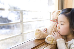 Girl looking outside from the window holding teddy bear