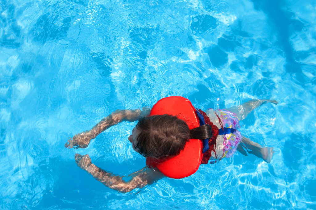 Little girl in life jacket swimming in swimming pool. Summer time.